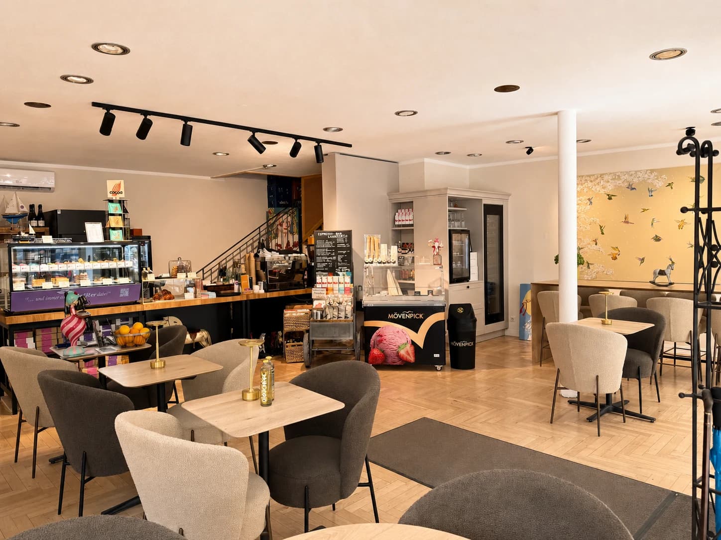 Heller Cafébereich mit Tischen, Sesseln und Verkaufstheke
