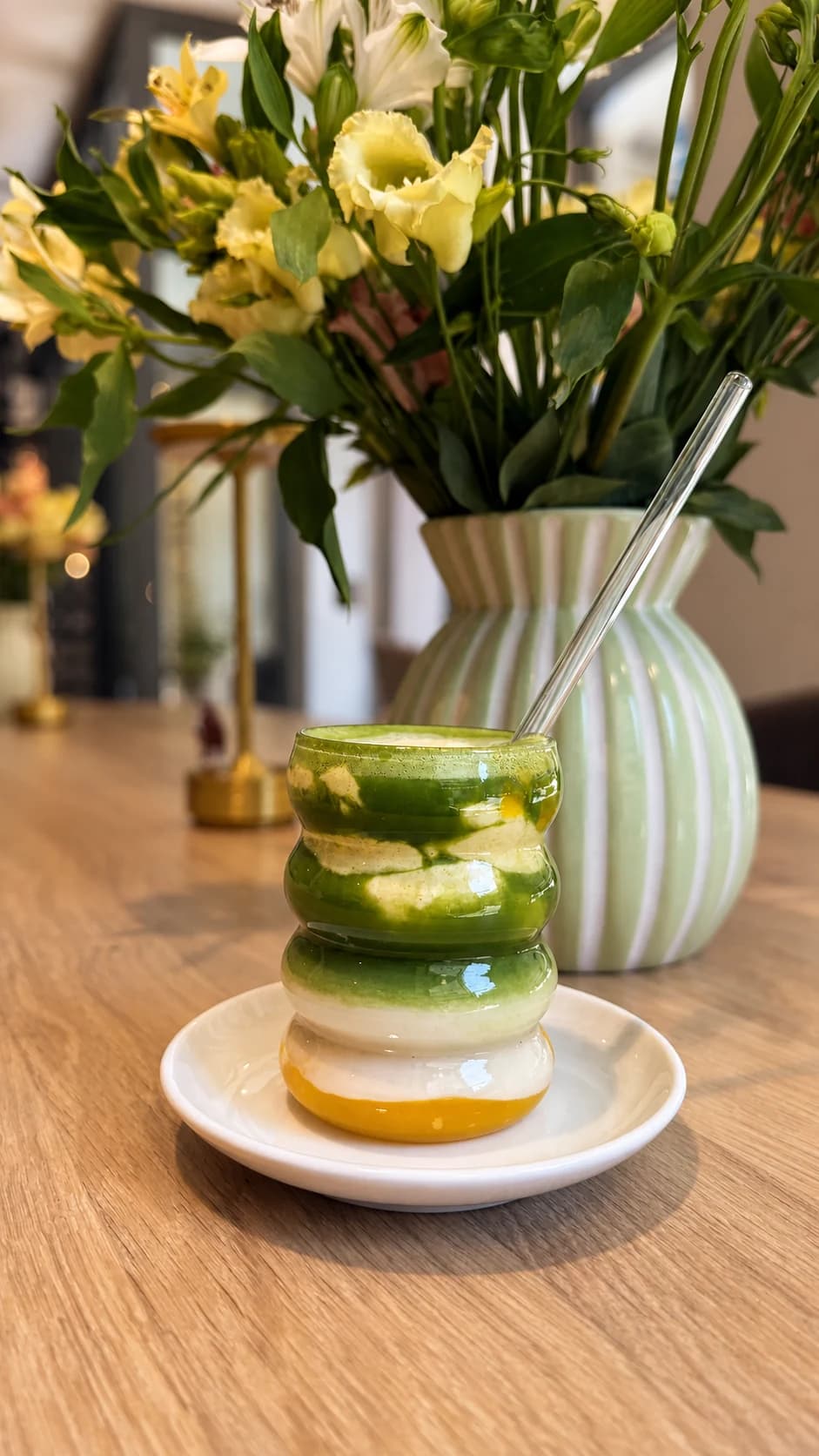 Geschichteter Matcha-Drink vor einem Blumenstrauß im Café